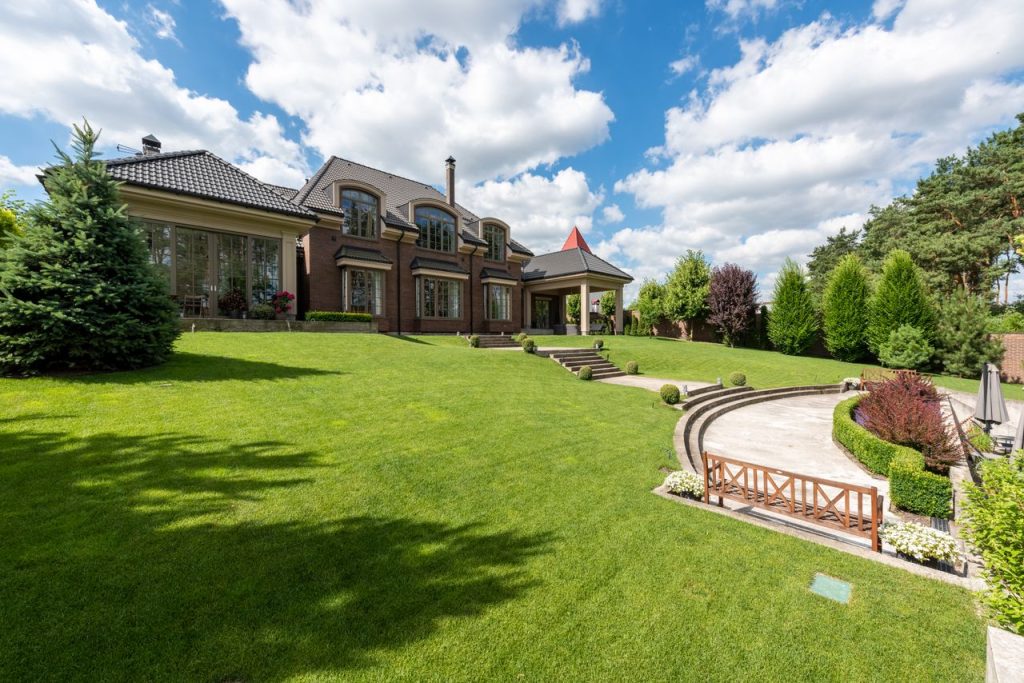 stats-img Elegant brick mansion with manicured lawn and garden under a bright blue sky.
